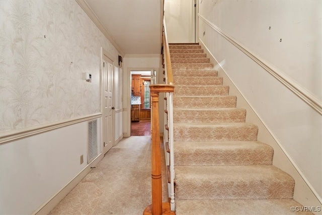 staircase featuring visible vents, ornamental molding, wainscoting, carpet, and wallpapered walls