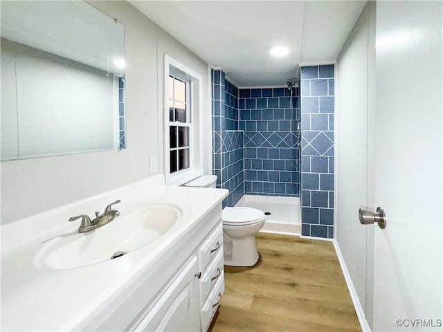 bathroom with tiled shower, vanity, hardwood / wood-style flooring, and toilet