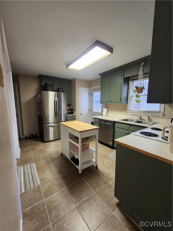 kitchen with dishwasher, sink, green cabinets, light tile patterned floors, and stainless steel fridge