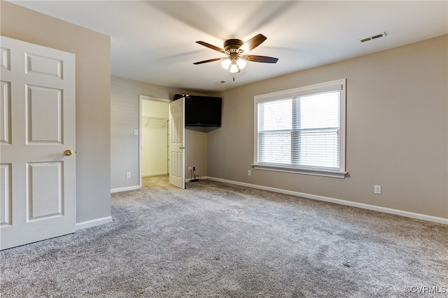 unfurnished bedroom featuring baseboards, visible vents, light colored carpet, ceiling fan, and a spacious closet