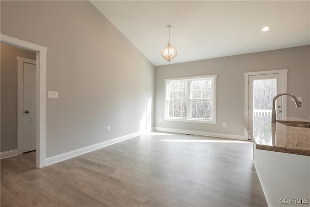 unfurnished dining area with vaulted ceiling, an inviting chandelier, sink, and light wood-type flooring