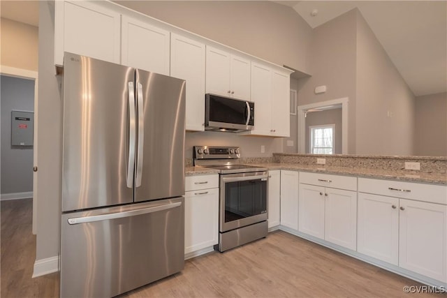 kitchen with vaulted ceiling, white cabinets, light stone counters, light hardwood / wood-style floors, and stainless steel appliances