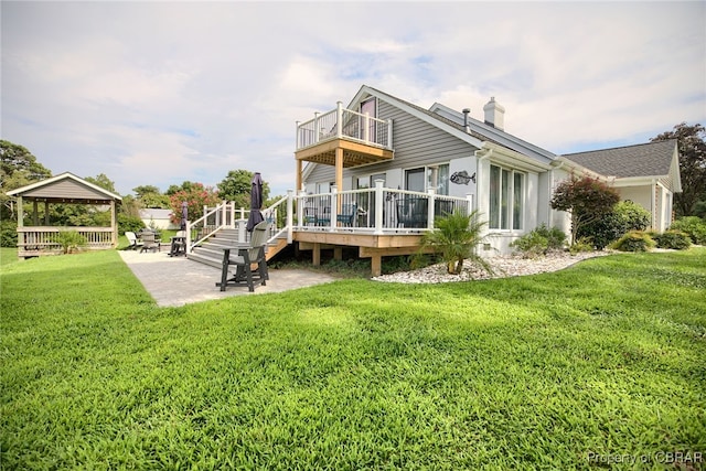 rear view of property featuring a balcony, a deck, a gazebo, a patio, and a lawn