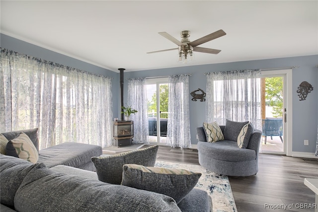 living room featuring ceiling fan, a wood stove, dark wood-type flooring, and a wealth of natural light