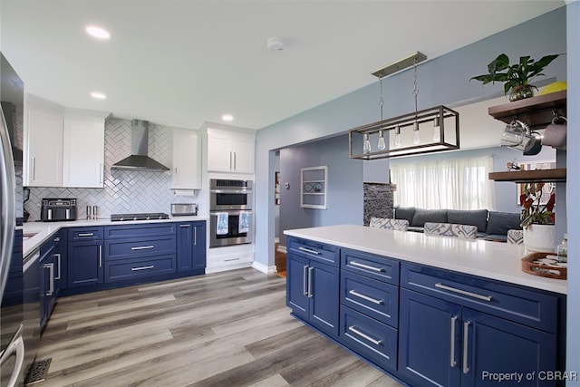 kitchen with blue cabinetry, appliances with stainless steel finishes, white cabinetry, and wall chimney range hood