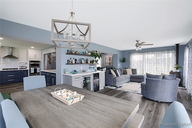 dining area featuring ceiling fan with notable chandelier, dark hardwood / wood-style floors, and beverage cooler