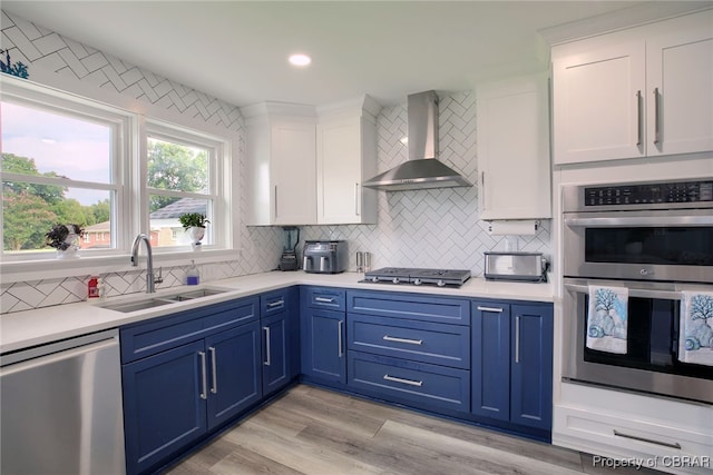 kitchen with white cabinetry, wall chimney exhaust hood, stainless steel appliances, light hardwood / wood-style flooring, and blue cabinets