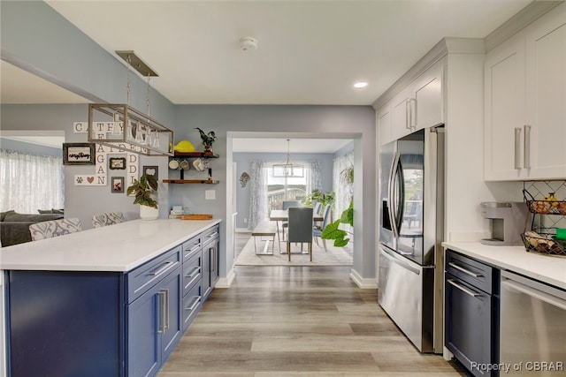 kitchen with appliances with stainless steel finishes, blue cabinets, pendant lighting, light hardwood / wood-style floors, and white cabinetry