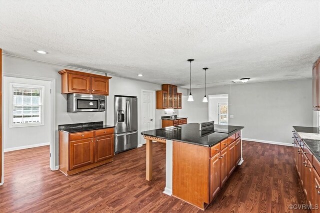 kitchen featuring appliances with stainless steel finishes, brown cabinetry, dark wood finished floors, and a kitchen island