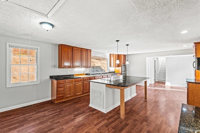 kitchen featuring a center island, a kitchen bar, a textured ceiling, decorative light fixtures, and dark hardwood / wood-style flooring