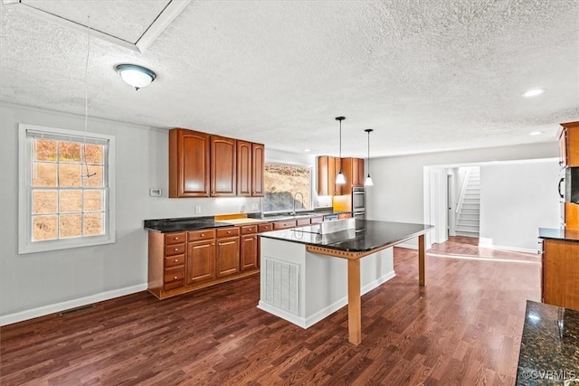 kitchen featuring dark wood-style floors, dark countertops, brown cabinetry, a sink, and a kitchen breakfast bar