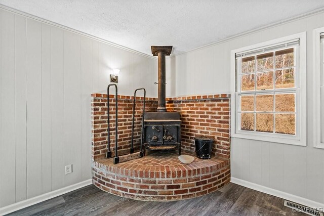 interior space featuring dark hardwood / wood-style flooring, ornamental molding, a textured ceiling, a wood stove, and wood walls