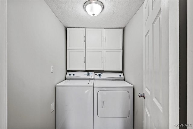 washroom featuring a textured ceiling, washing machine and clothes dryer, and cabinet space