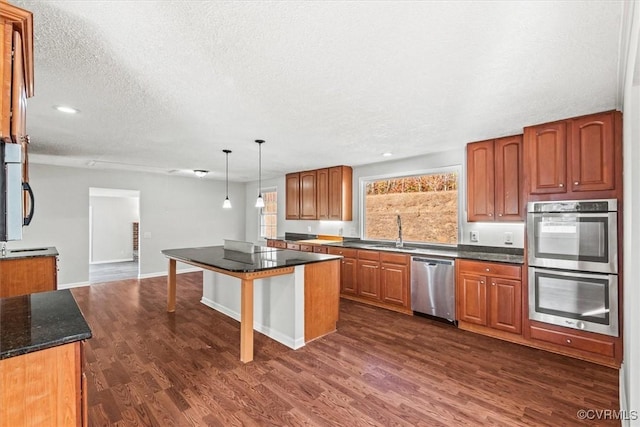 kitchen with dark wood-style floors, hanging light fixtures, appliances with stainless steel finishes, brown cabinetry, and a sink