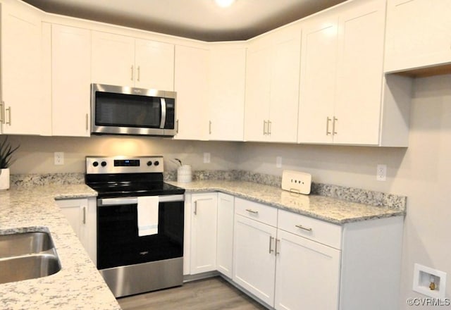 kitchen featuring stainless steel appliances, light wood finished floors, white cabinetry, and light stone counters