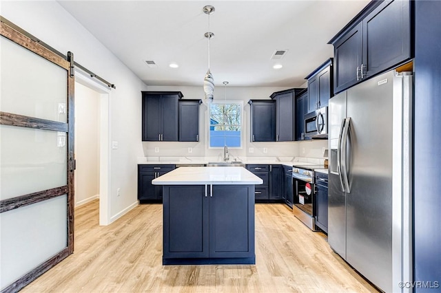 kitchen with hanging light fixtures, stainless steel appliances, a barn door, light hardwood / wood-style floors, and a kitchen island