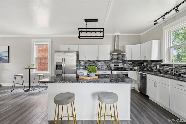 kitchen featuring wall chimney exhaust hood, a kitchen island, stainless steel appliances, and decorative light fixtures