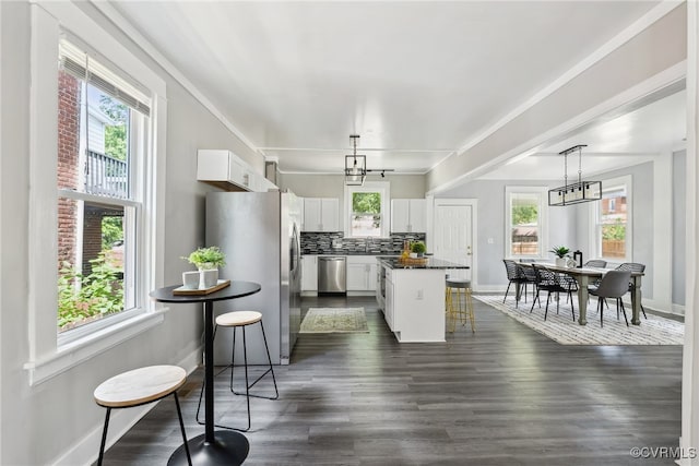 kitchen featuring decorative backsplash, appliances with stainless steel finishes, a center island, white cabinetry, and hanging light fixtures