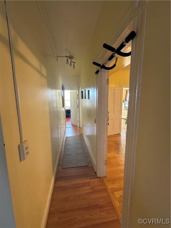 corridor with wood-type flooring and vaulted ceiling