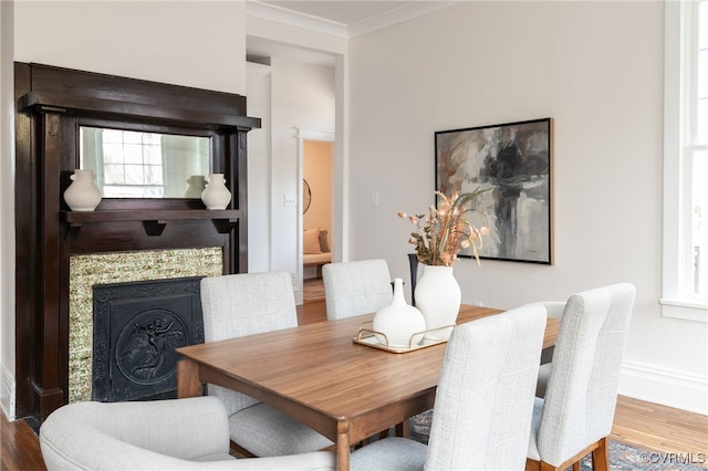 dining area with crown molding, a healthy amount of sunlight, wood finished floors, a tile fireplace, and baseboards