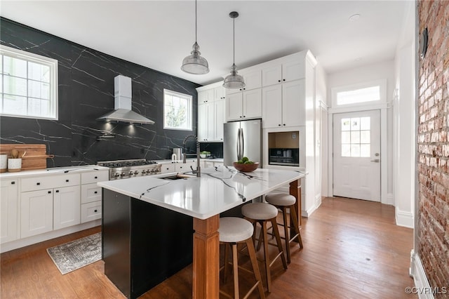 kitchen featuring stainless steel appliances, a sink, light wood-style floors, wall chimney range hood, and decorative backsplash