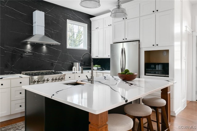 kitchen featuring light wood finished floors, white cabinets, wall chimney exhaust hood, stove, and freestanding refrigerator