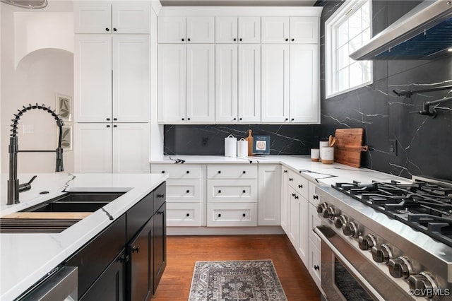 kitchen with stainless steel appliances, wood finished floors, a sink, white cabinets, and wall chimney exhaust hood