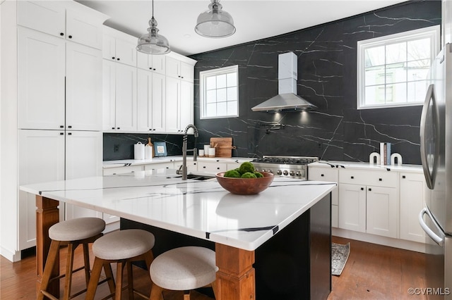 kitchen featuring a healthy amount of sunlight, wall chimney range hood, wood finished floors, and freestanding refrigerator