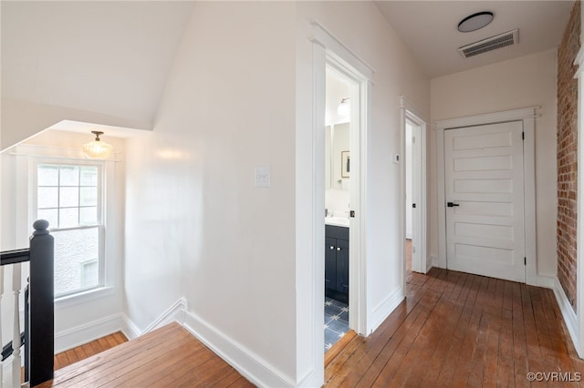 corridor featuring wood-type flooring, visible vents, baseboards, and an upstairs landing