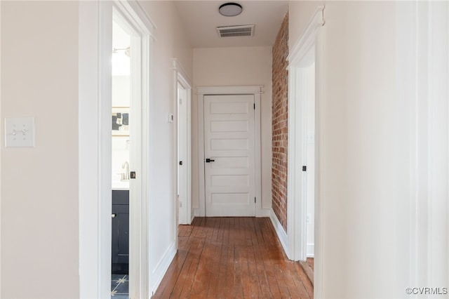 hall featuring baseboards, visible vents, brick wall, and hardwood / wood-style flooring