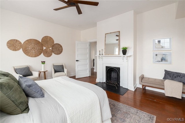 bedroom with baseboards, a ceiling fan, a fireplace with raised hearth, and wood finished floors