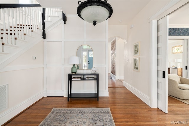 corridor featuring baseboards, stairway, arched walkways, and wood finished floors