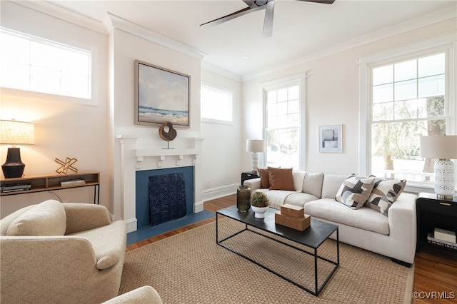 living area with baseboards, a fireplace with flush hearth, ceiling fan, wood finished floors, and crown molding