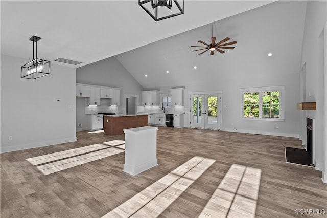 unfurnished living room featuring hardwood / wood-style flooring, ceiling fan with notable chandelier, and high vaulted ceiling