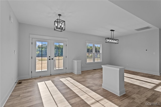 unfurnished dining area with french doors, light wood-type flooring, and an inviting chandelier