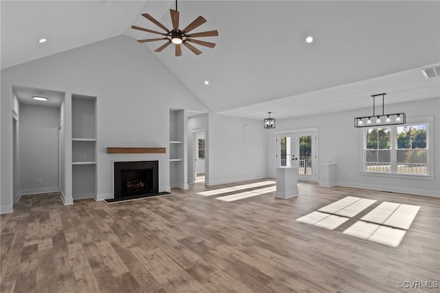 unfurnished living room featuring french doors, ceiling fan with notable chandelier, light hardwood / wood-style flooring, and high vaulted ceiling