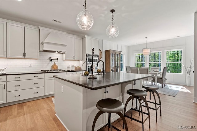 kitchen with hanging light fixtures, a center island with sink, white cabinetry, and premium range hood