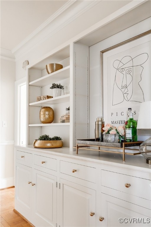 bar featuring white cabinets, light hardwood / wood-style floors, and crown molding