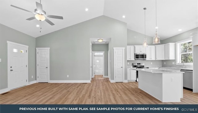 kitchen with a center island, stainless steel appliances, hanging light fixtures, white cabinets, and light wood-type flooring