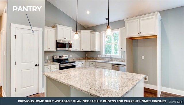 kitchen with light stone counters, white cabinets, hanging light fixtures, appliances with stainless steel finishes, and a center island