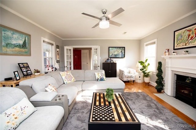 living room with crown molding, a fireplace, ceiling fan, and light wood-type flooring