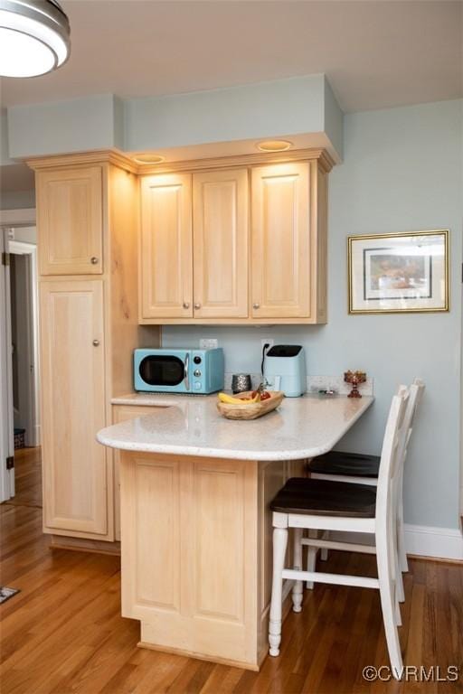 kitchen with a kitchen breakfast bar, kitchen peninsula, light brown cabinets, and hardwood / wood-style floors