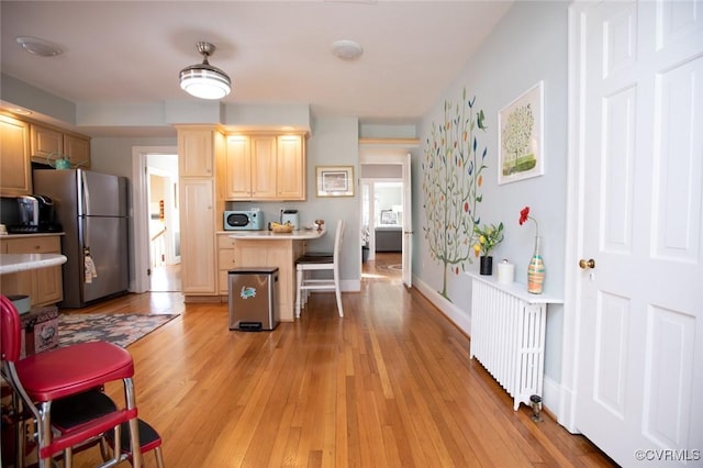 kitchen featuring light brown cabinets, a breakfast bar area, radiator heating unit, a kitchen island, and stainless steel refrigerator