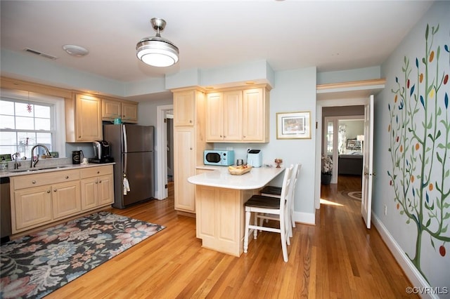 kitchen featuring light brown cabinetry, light wood-type flooring, a breakfast bar, stainless steel appliances, and sink