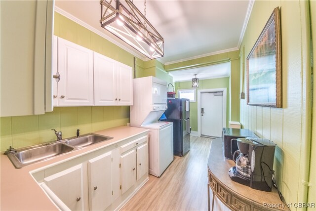 kitchen with white cabinets, sink, stacked washer and dryer, hanging light fixtures, and light wood-type flooring