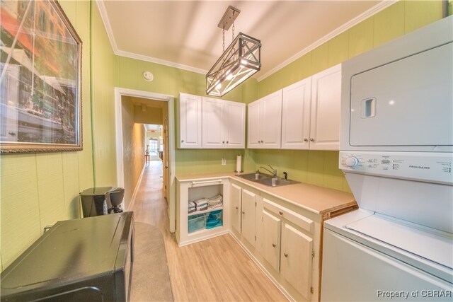 clothes washing area featuring cabinets, sink, crown molding, stacked washing maching and dryer, and light wood-type flooring