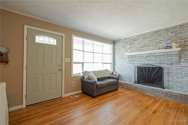 unfurnished living room with a brick fireplace, a textured ceiling, light hardwood / wood-style flooring, and brick wall