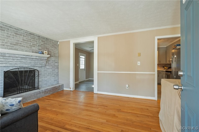 living room featuring ornamental molding, a textured ceiling, ceiling fan, a fireplace, and light hardwood / wood-style floors