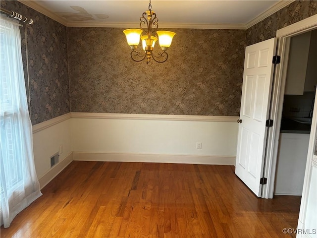 spare room featuring hardwood / wood-style floors, an inviting chandelier, and crown molding