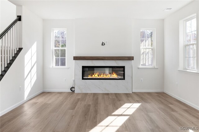 unfurnished living room featuring a premium fireplace, plenty of natural light, and light hardwood / wood-style floors